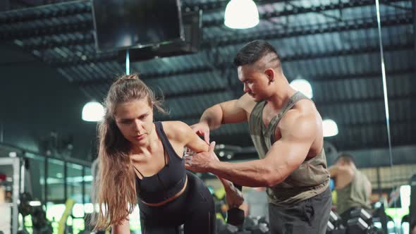 Asian Fitness trainer motivate and support young sportswoman lift weight dumbbell at gym health club