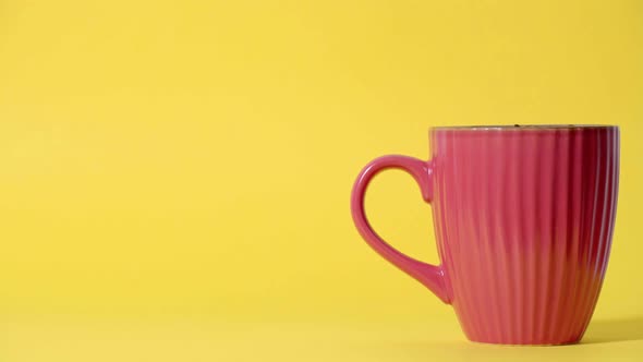 A reddish ceramic coffee mug taken by a hand, yellow backdrop in the background - static studio shot