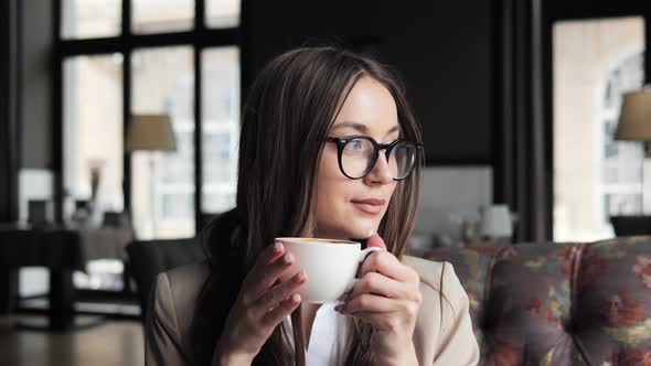 Beautiful Pensive Business Woman in Eyeglasses Drinking Coffee in Hotel Lounge