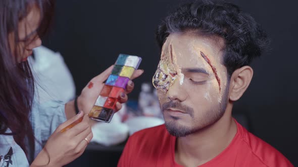 Professional make up artist coloring mask on man's face for Halloween party