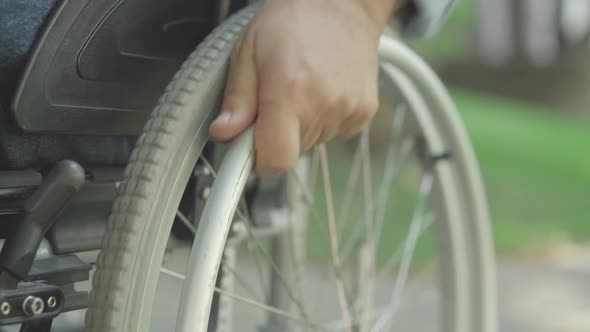 Close-up of Old Male Caucasian Hand Rolling Wheelchair. Unrecognizable Handicapped Man Riding