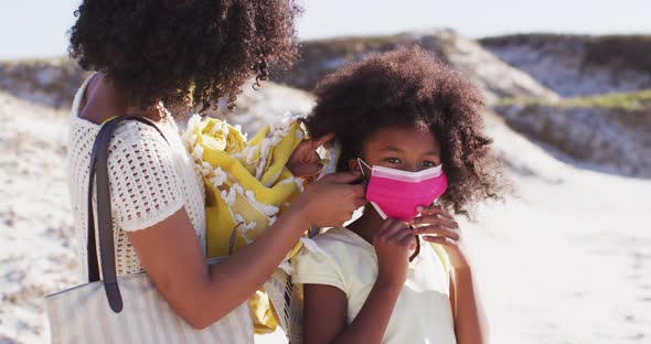 African american mother putting face masks on daughters face on the beach