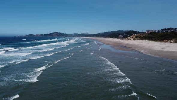 Zoom-in drone shot flying over waves at Nye Beach on the Oregon coast in the small town of Newport.