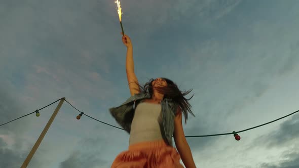 Low angle view of happy woman jumping with firework candle