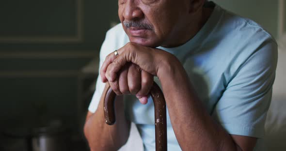 Senior mixed race man sitting thinking, leaning on walking stick