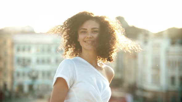 A Young Attractive Smiling Woman with Curly Hair Making a Turn and Looking in the Camera