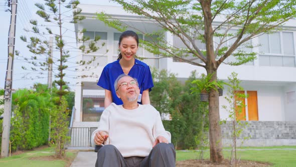 Asian caregiver nurse take care senior male sit on wheelchair outdoor.