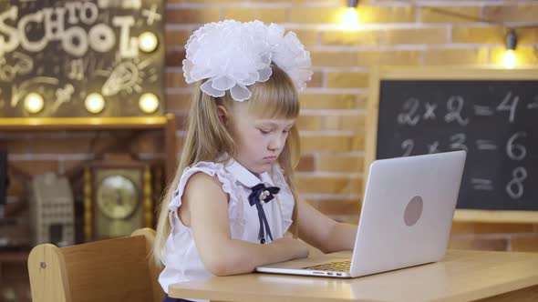 Little Girl Sits at Table and and Typing on the Laptop Keyboard on the Background of a School Class