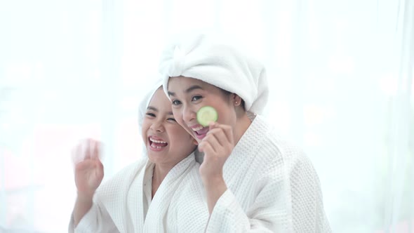 Happy nice positive mother and daughter lying together and smiling while doing a cucumber mask.