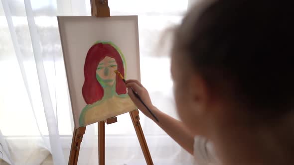 Beautiful Young Artist Paints a Portrait with Oil Paints Sitting at Home in Front of the Window