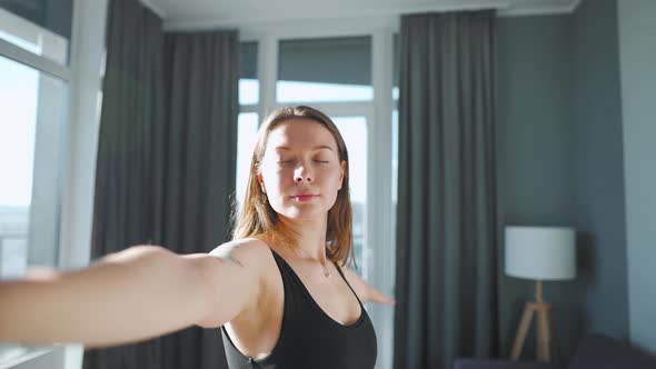 Young Caucasian Woman in Black Jumpsuit Doing Yoga Virabhadrasana at Home to Develop Flexibility and