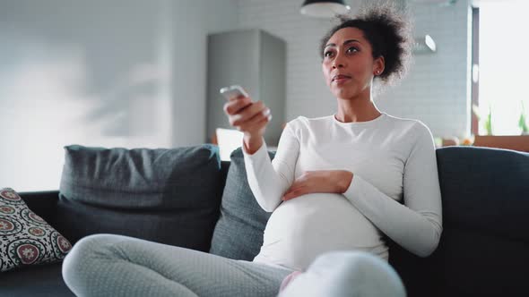 Handsome African pregnant woman switching channels on TV