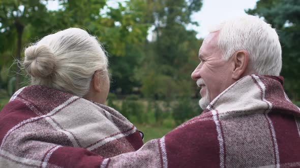 Mature Couple Sitting on Bench in Park and Warming Under Plaid, Back View