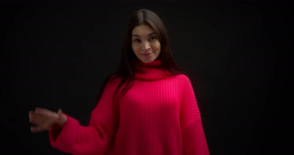 Smiling Asian Woman in a Bright Pink Sweater Waves Her Hand