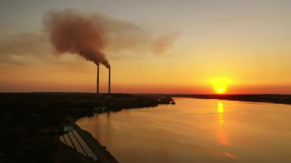 Orange sunset over the water. Harmful plant with industrial pipes near the river. 