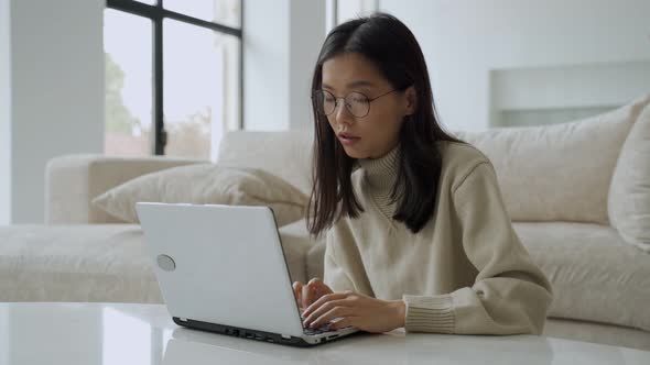 A Successful Asian Businesswoman with Glasses Enjoys Success with a Laptop on Her Desktop