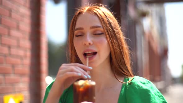 Closeup Face of Attractive Smiling Young Woman Drinking Cocktail Through Straw Sitting at Table in