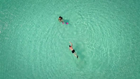 Aerial view of man and woman swimming with masks and flippers in clear sea.