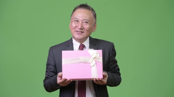 Mature Japanese Businessman with Gift Box Against Green Background