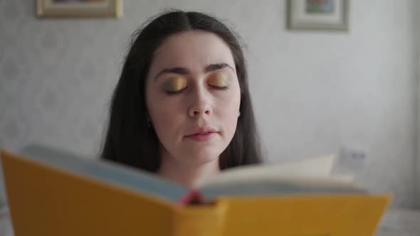 A Young Woman Reads a Book and Rubs Her Eyes with Fatigue and Irritation