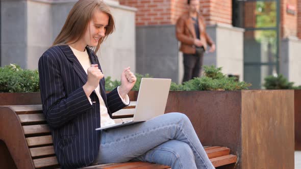 Excited Woman Celebrating Success on Laptop Sitting on Bench