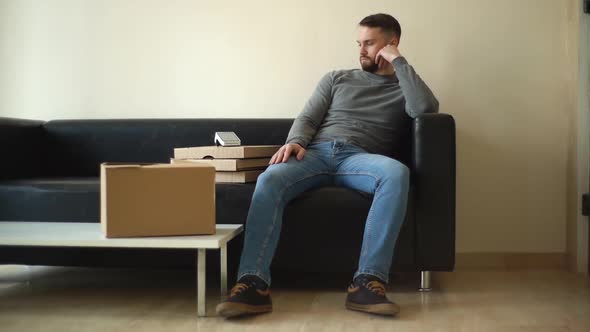 Tired Delivery Man in Casual Clothes Waiting for Client While Sitting on Sofa in Spacious Lobby