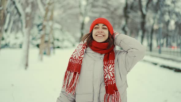 Slow Motion Cheerful Woman in Red Cap and Mittens Enjoying First Snow in Winter Park in January