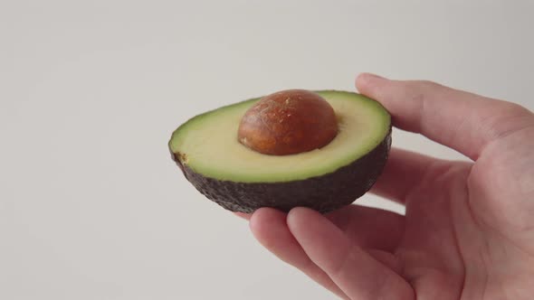 Hand of a Man Holding a Sliced Half of a Fresh Juicy Avocado on a White Background