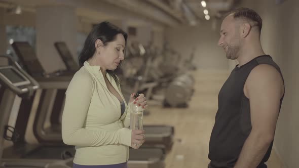 Positive Adult Man and Woman Talking in Gym and Laughing. Side View Portrait of Athletic Sportive