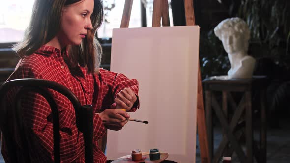 A Young Woman in Art Workshop Opens Up Jars of Color Paints Sitting on Front of an Easel