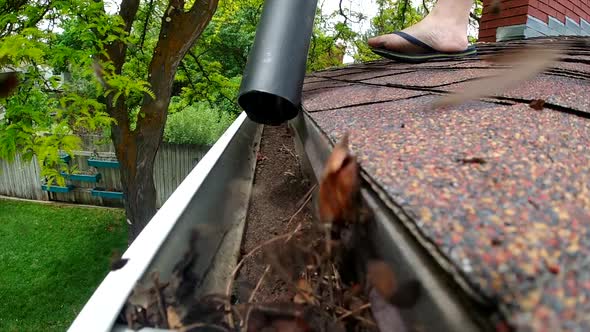 A leaf blower is seen blowing leaves and debris out of a rain gutter on a roof in slow motion.