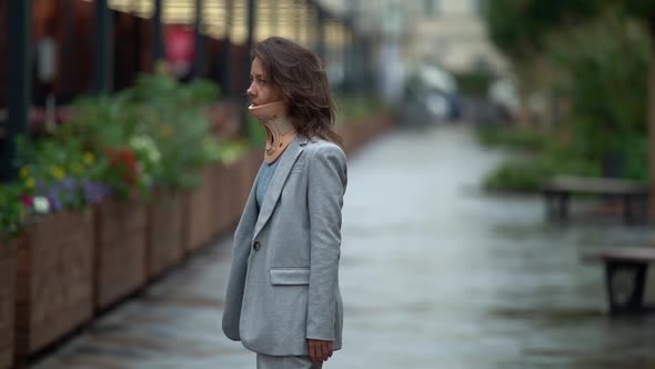 a Middleaged Woman with an Orthopedic Collar Around Her Neck and a Gray Suit Walks Against the