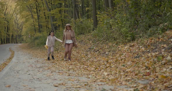 Young Mother with Her Daughter Running on Yellow Leaves