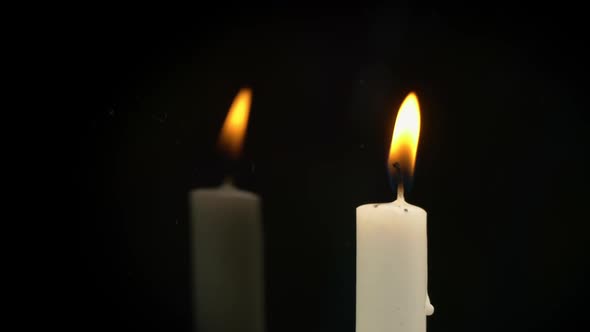 White Paraffin Candle with Yellow Tints Burns on Black Background in Reflection