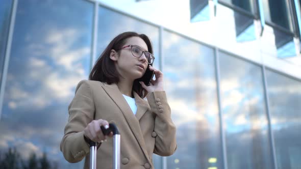 A Young Woman Stands Against the Background of a Business Center and Speaks on the Phone. Girl