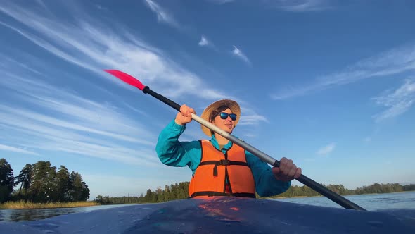 Young Man in Hat and Life Vest Rows Paddle Sitting in Boat