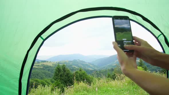 Girl takes pictures on a smartphone beautiful mountain landscape with a tent at sunset.