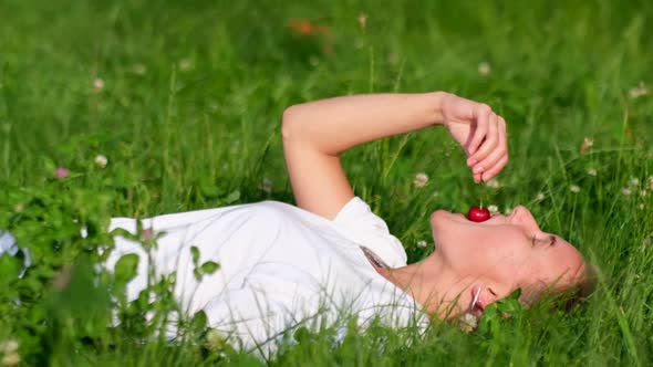 Beautiful Young Woman Lying on the Grass Enjoying Cherries
