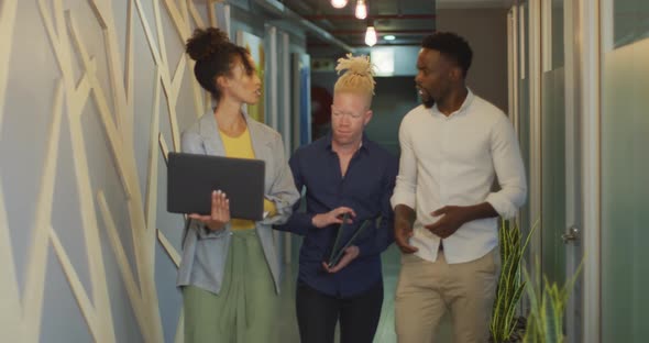 Diverse business people discussing with laptop and walking in creative office