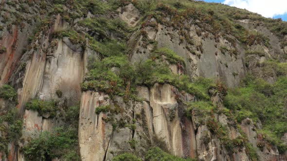 Approaching a cliff with grey brown and red colors that is covered in grass and bromelias