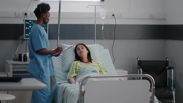 Afro American Asisstant Checking Sick Woman While Sitting in Bed in Hospital Ward