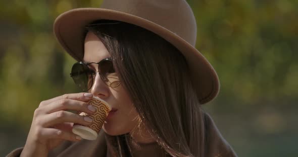Close-up Face of an Elegant European Woman in Brown Hat and Sunglasses Drinking Tea or Coffee