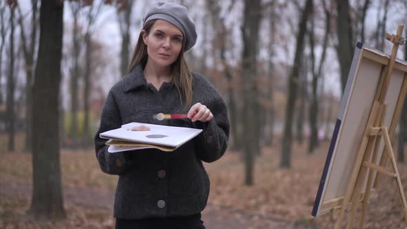 Portrait of Confident Attractive Young Woman Posing with Painting Palette in Autumn Park at Easel