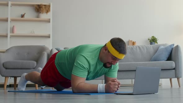 Chubby Man Exercising at Home Greeting Coach Via Video Call on Laptop and Doing Plank Exercising in