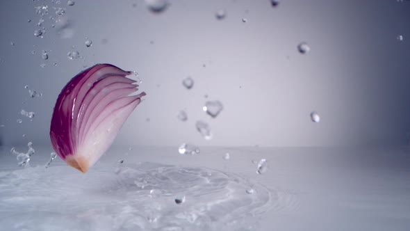 Cut red onion falling on water surface. Slow Motion.