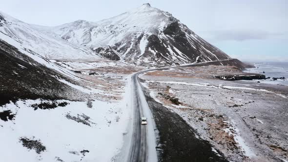 Aerial following flight behind driving white van on Djúpivogur route with massive snowy mountains at