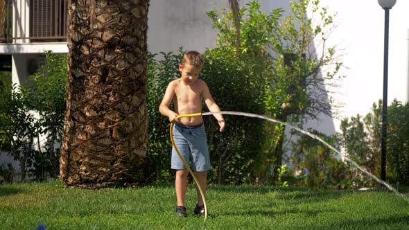 Boy trying to cope with water jet when watering lawn