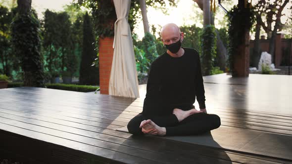 Barefoot Man in Black Mask and Sportswear is Performing Yoga Sitting in Lotus Pose on Mat at