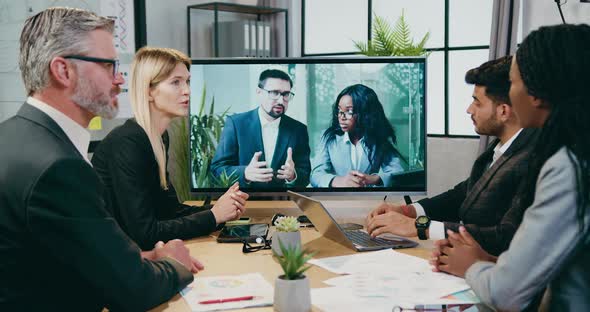 Businesspeople Advising Between Themselves During Video Conference with their Male and Female