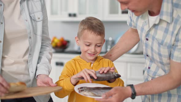 Seafood Joyful Little Boy Chooses Fish for Snack with Mom and Dad at Home on Kitchen Background